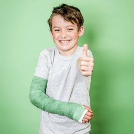 cool young schoolboy with broken arm and green arm plaster posing in front of green background